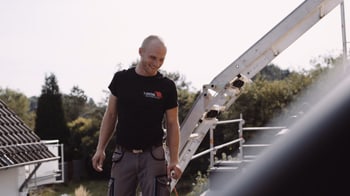 Lächelnder Handwerker auf einem Dach neben einer Leiter.
