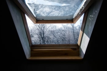 Blick aus einem Dachfenster auf schneebedeckte Bäume und einen klaren Winterhimmel.